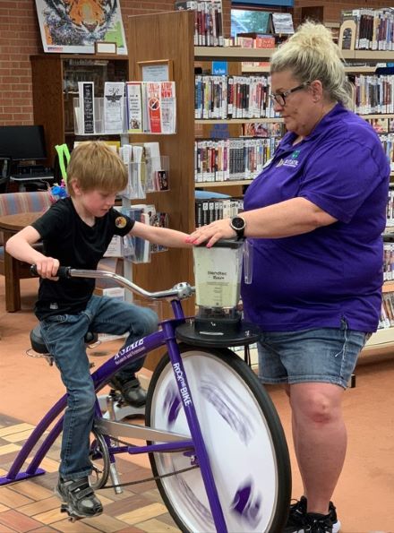 Anna Muir demonstrating healthy foods with the use of the blender bike at a summer library program for youth